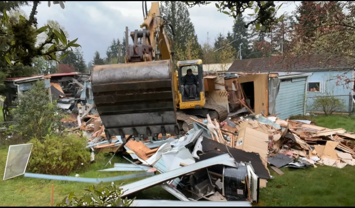 Variant Construction demolishing an old mobile home using heavy machinery.